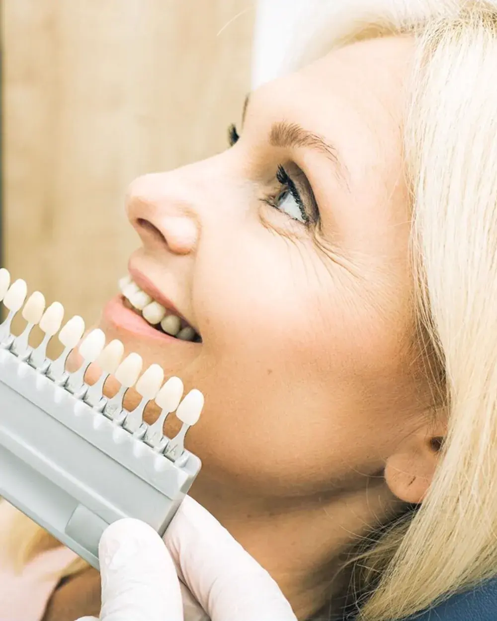 A dentist holding a tooth shade guide against a patient's smile